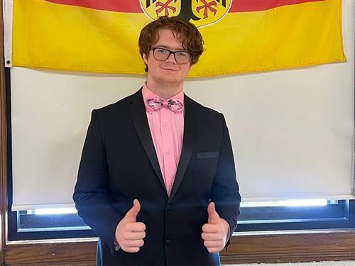 student stands in front of the German flag with thumbs up